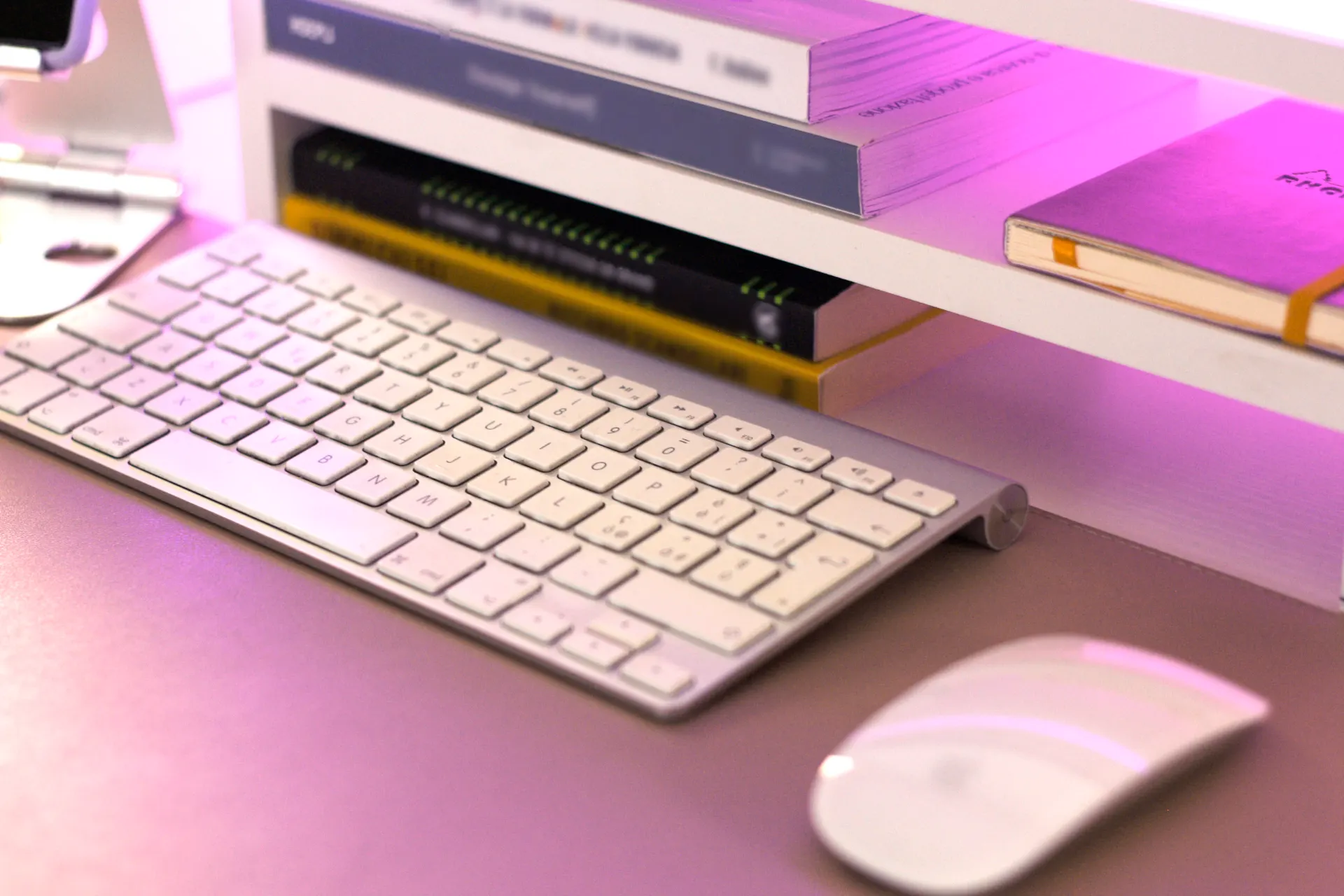 Tastiera e mouse bianchi su scrivania rosa con libri design in scaffale: setup per brand designer Monza e Brianza e template Canva per professionisti e PMI.